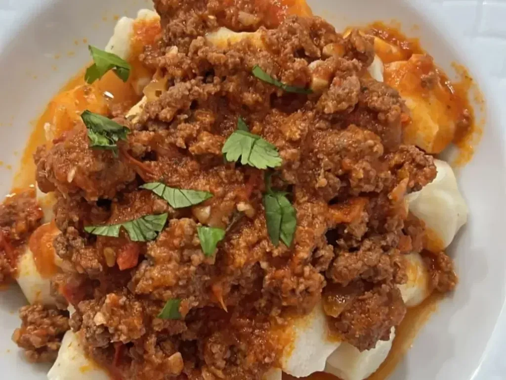 Gnocchi or dumplings with chunky red meat sauce and herbs.