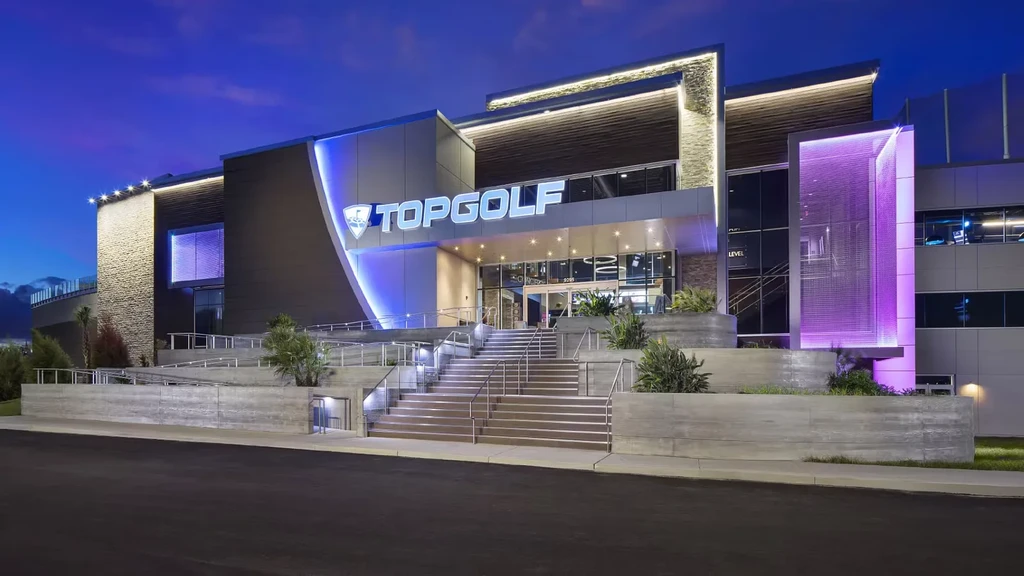Modern Topgolf exterior at night, illuminated by blue and purple LEDs.