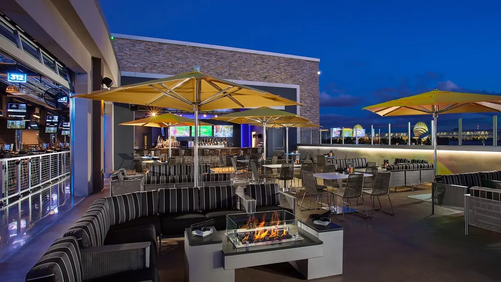 Lively rooftop bar at dusk, fire pit, lounge, and golf bays.