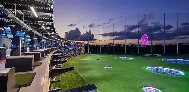 Topgolf-style driving range at dusk with glowing targets and a Ferris wheel.
