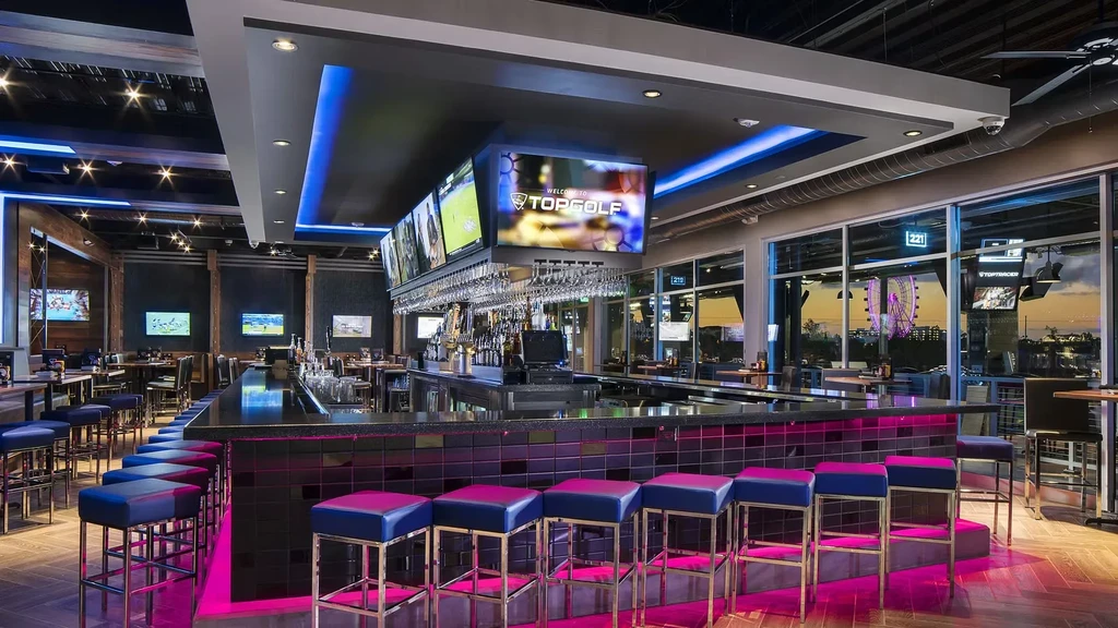 Vibrant Topgolf bar with pink LED light, TVs, and Ferris wheel.