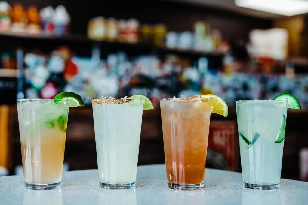Four distinct iced drinks with various garnishes on a light counter.