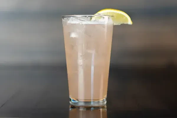 Tall glass of pink effervescent drink with lime on ice.