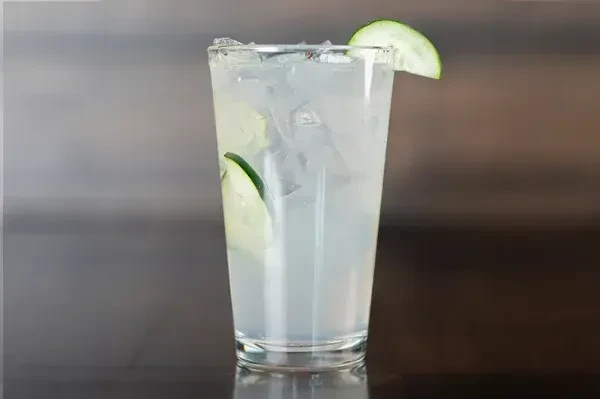 Clear glass with iced light drink and cucumber slices, one on rim.
