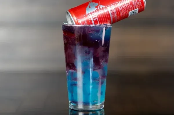 Layered blue and purple drink with ice, an inverted Red Bull can.