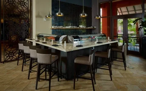 Modern sushi bar with unoccupied counter, ingredients, and tropical view.