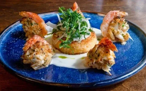 Artfully plated stuffed shrimp, seafood stuffing, polenta, greens, sauce.