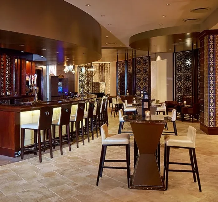 Sophisticated bar interior featuring a curved bar, cream stools, and patterned decor.