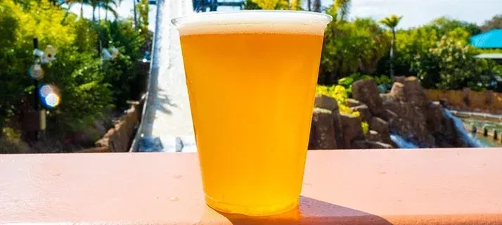 Golden beer in a plastic cup with frothy head, tropical background.