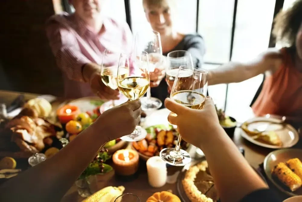 Hands clinking white wine glasses over a blurred, festive table.