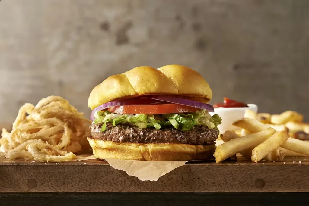 Gourmet burger, onion rings, French fries, and ketchup on a wooden board.