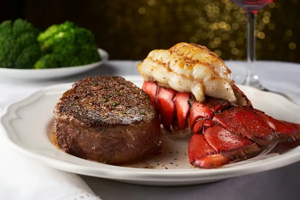 Close-up: Gourmet seared steak and lobster with broccoli and wine.