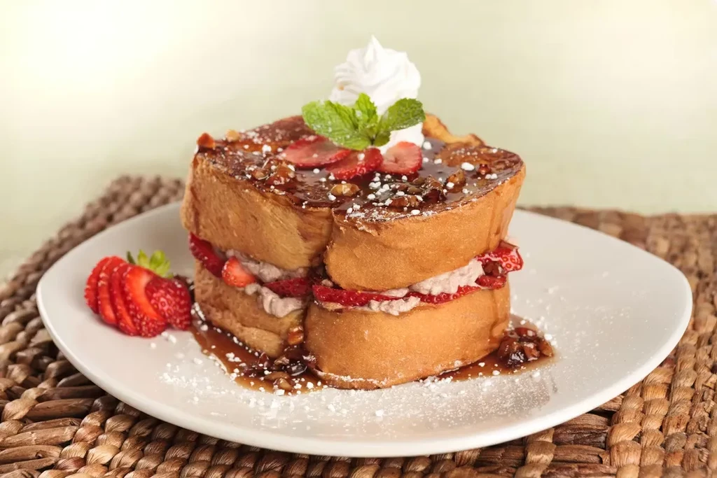 Thick-cut French toast layered with cream, strawberries, syrup, and whipped cream.