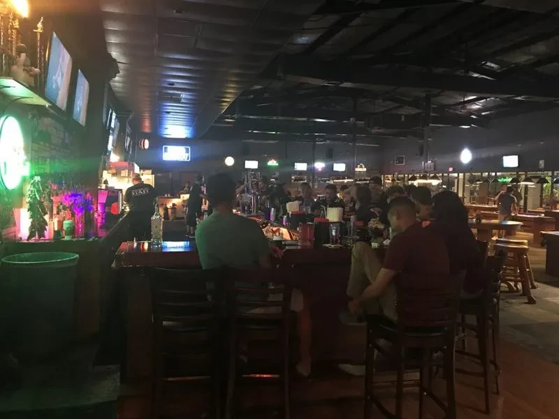 Patrons and staff in a dimly lit bar with pool tables and TVs.