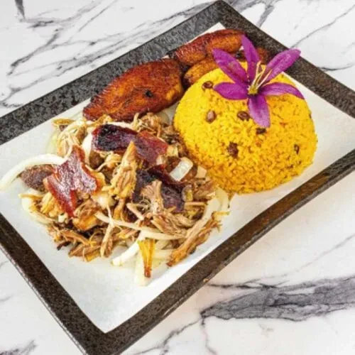 Shredded pork, yellow rice, fried plantains, garnished with a purple orchid.