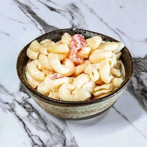 Macaroni salad with pimento in an earthy bowl on marble surface.
