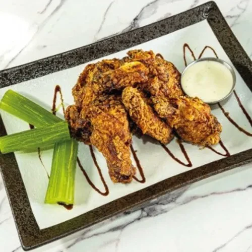Plate of crispy fried chicken wings, celery, and creamy dipping sauce.