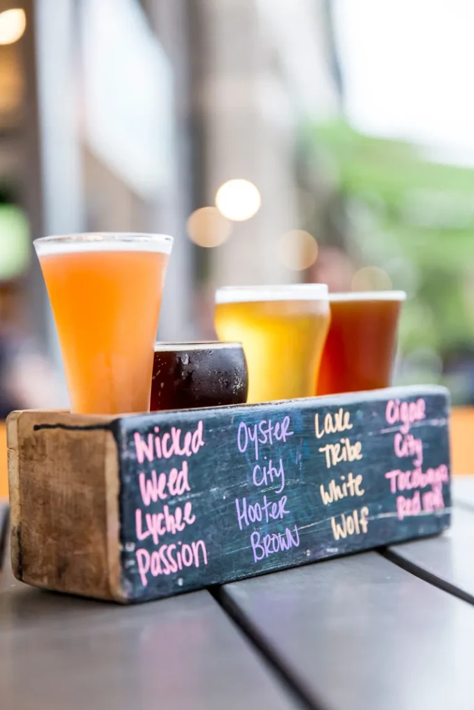 Flight of four craft beers on a rustic labeled wooden tray.