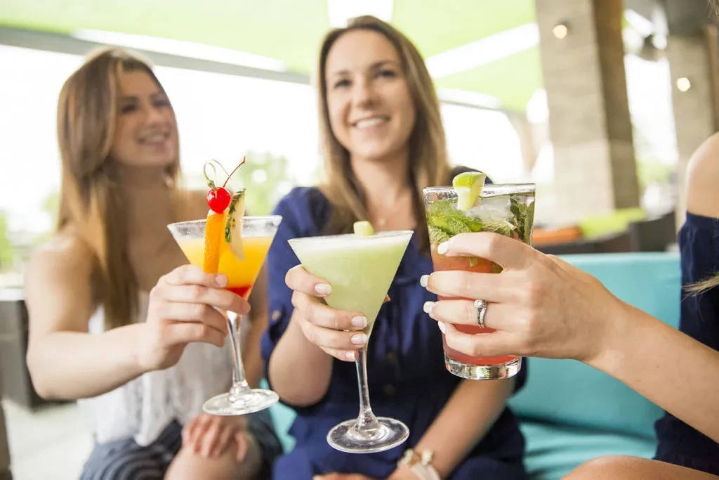 Three women toasting colorful cocktails in a social setting.