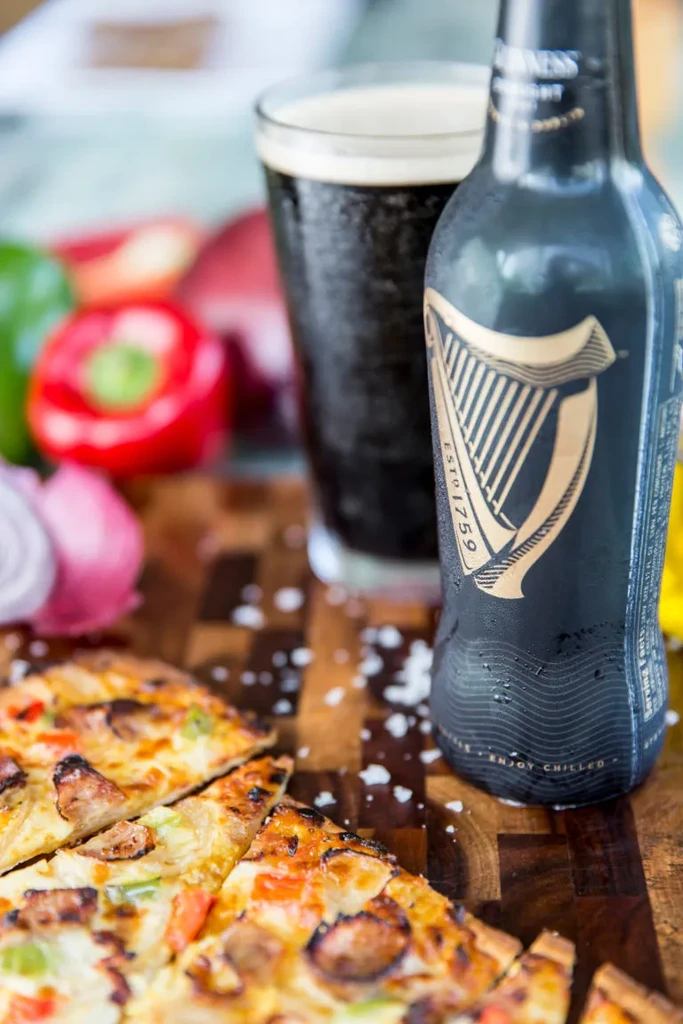 Guinness beer, full glass, and pizza with vegetables on wood.