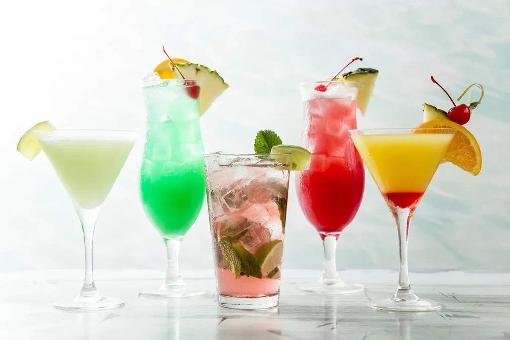Five vibrant, garnished cocktails in various glasses on a reflective surface.