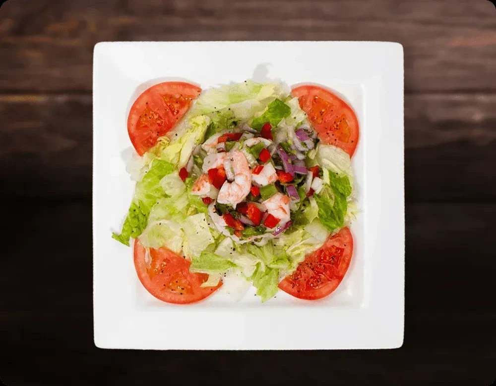 Overhead: Green lettuce, red tomatoes, and shrimp ceviche on a white plate.