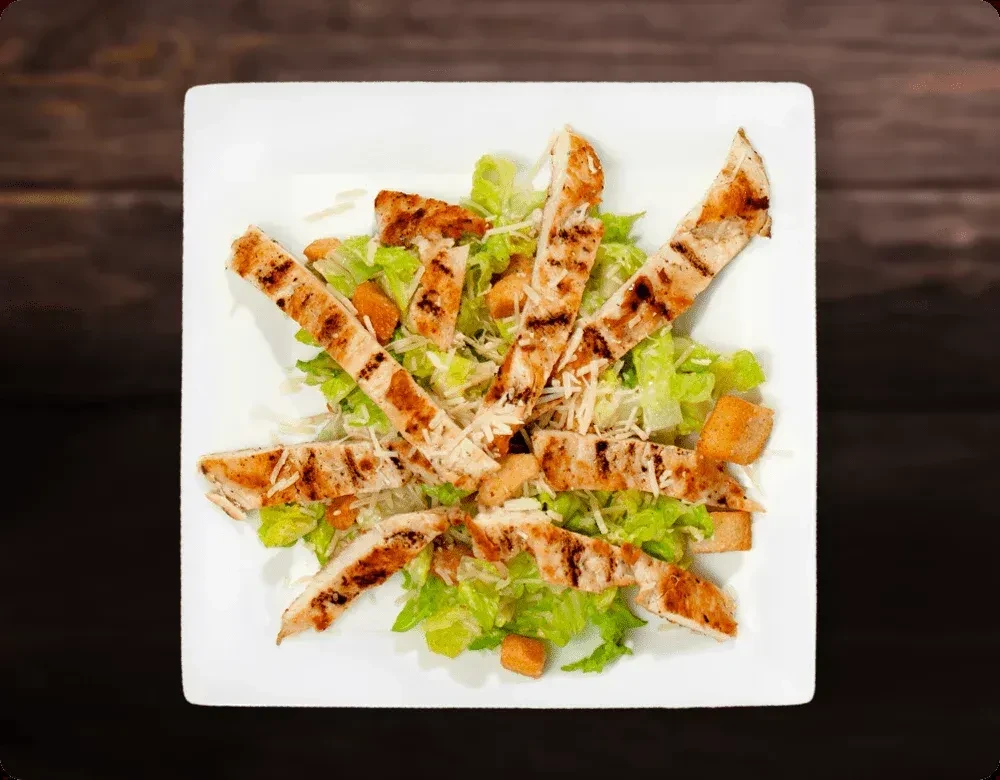 Grilled chicken Caesar salad with croutons and parmesan, overhead view.