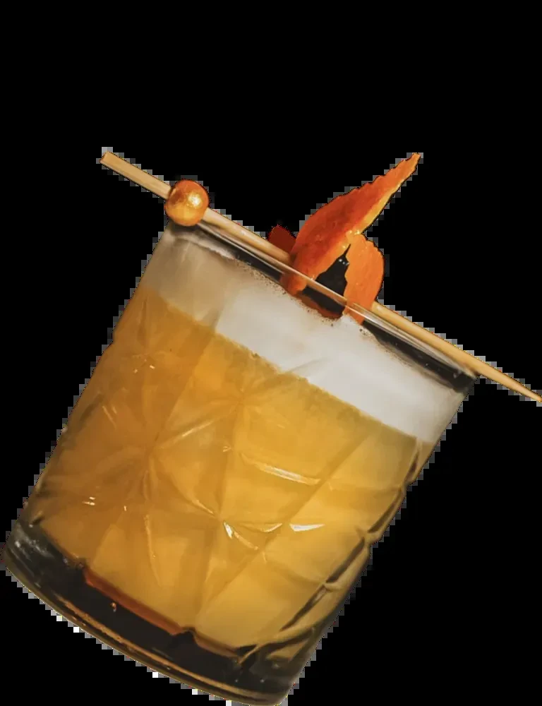 Faceted glass with amber cocktail, foam, orange peel, and gold sphere.