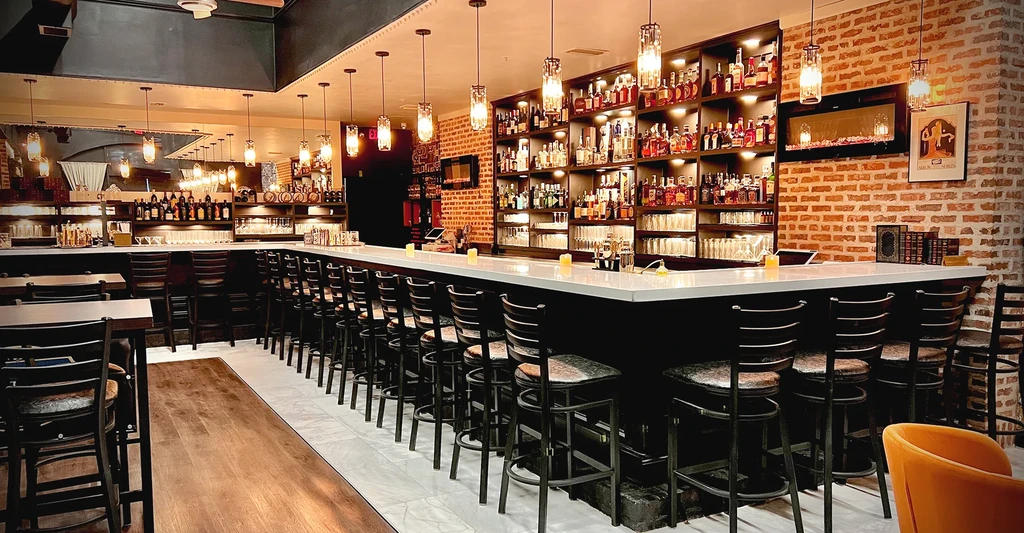 Upscale bar interior: L-shaped bar, liquor display, red brick walls, empty.