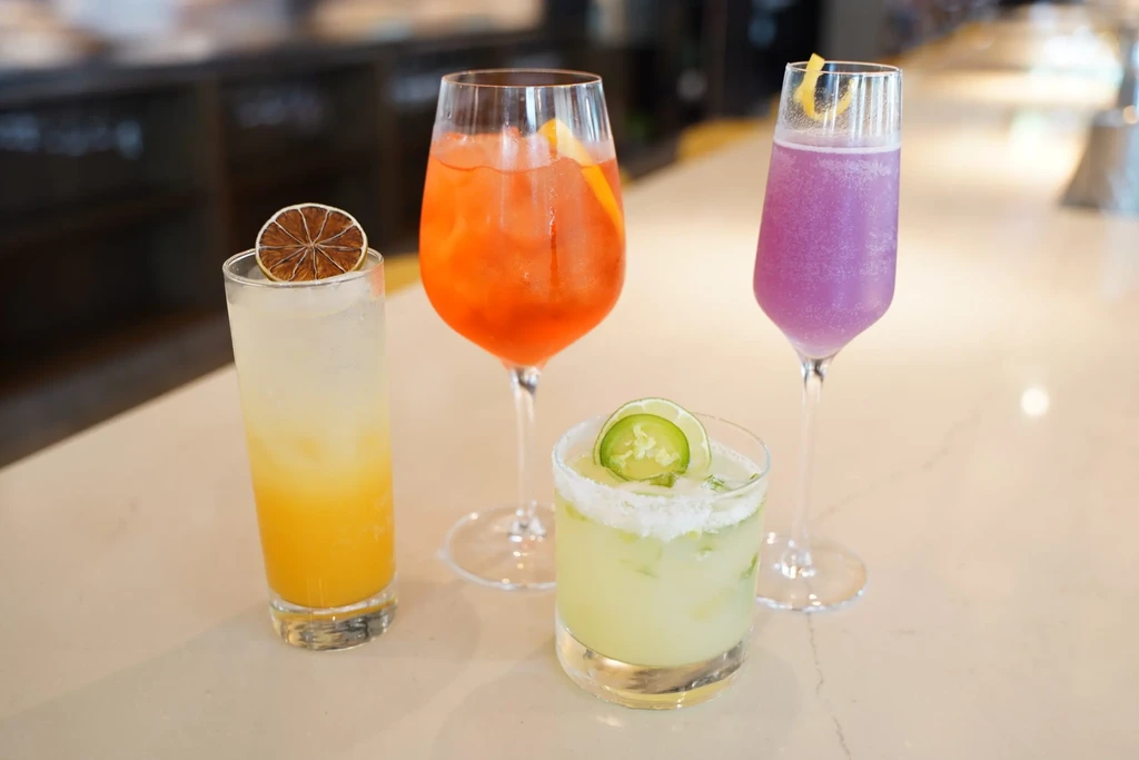 Four distinct cocktails with various garnishes on a bar counter.