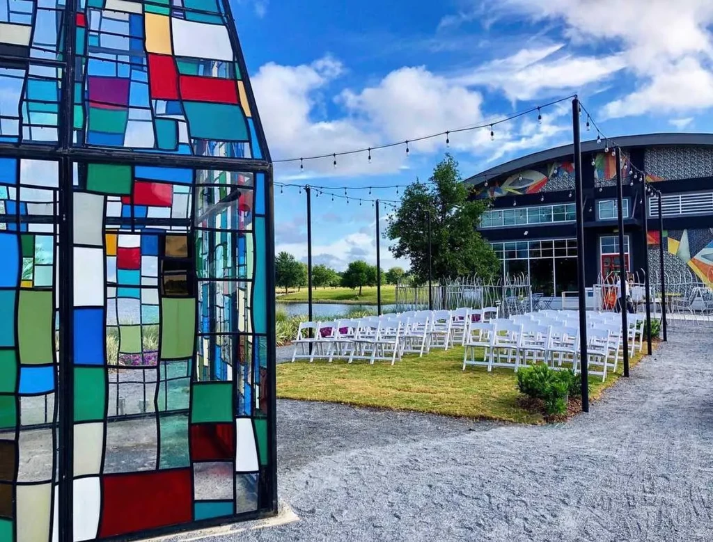 Vibrant stained-glass art, outdoor chairs, lake, and modern building.
