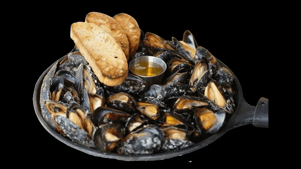 Cooked mussels in a pan with golden sauce, toasted bread.