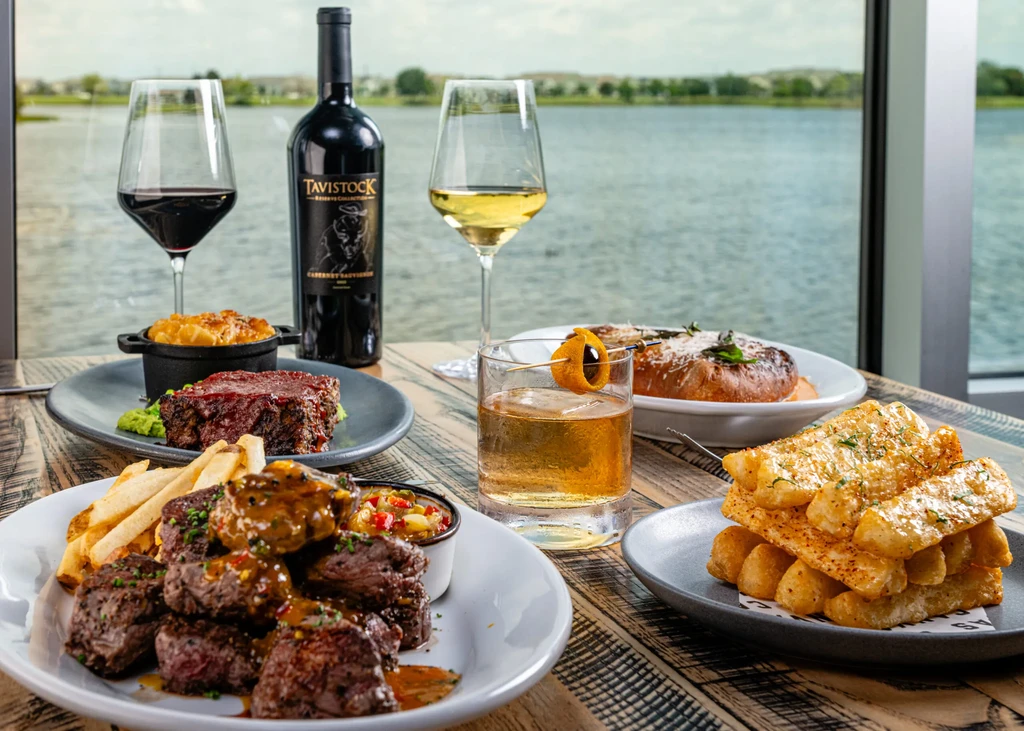 Table laden with gourmet food and drinks overlooking a lake.