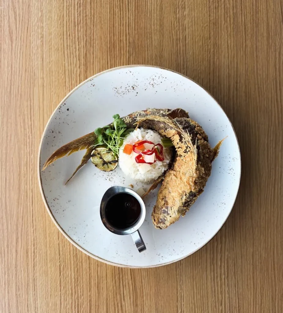 Plate of crispy fried fish, rice, grilled lime, and dark sauce.
