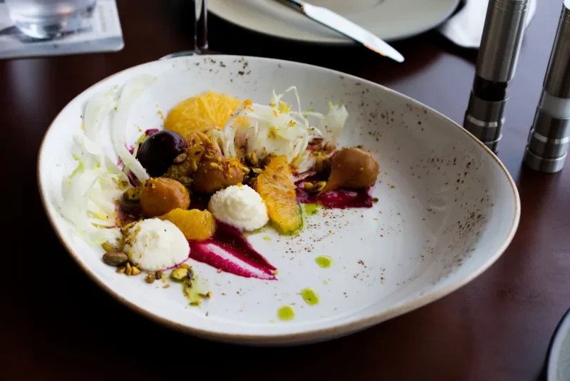 Artfully plated gourmet dish with citrus, vegetables, sauce, and pistachios.