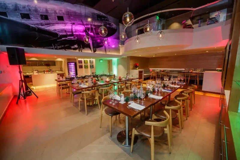 Restaurant interior with purple-lit airplane mural and dynamic colored lighting.