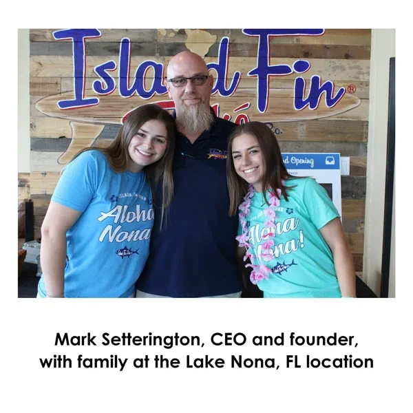 Three people, a man and two women, smiling before an "Island Fin" sign.