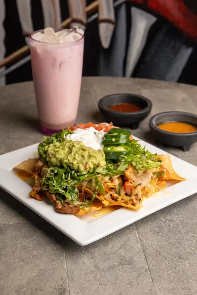 Loaded nachos, pink drink, and sauces on a table.