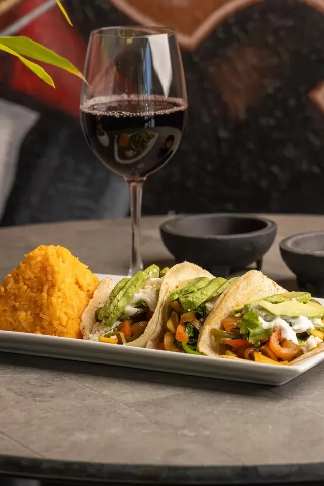 Colorful vegetable tacos, seasoned rice, and a glass of red wine.