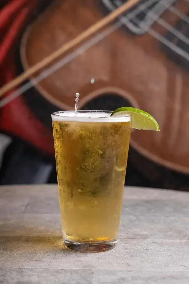 Cold bubbly amber drink with lime and splash, instrument mural background.