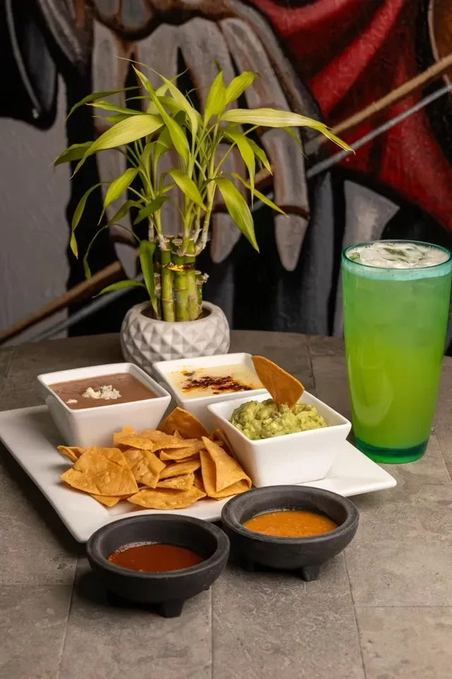 Mexican chips, guacamole, cheese dips, salsas, and a green drink.