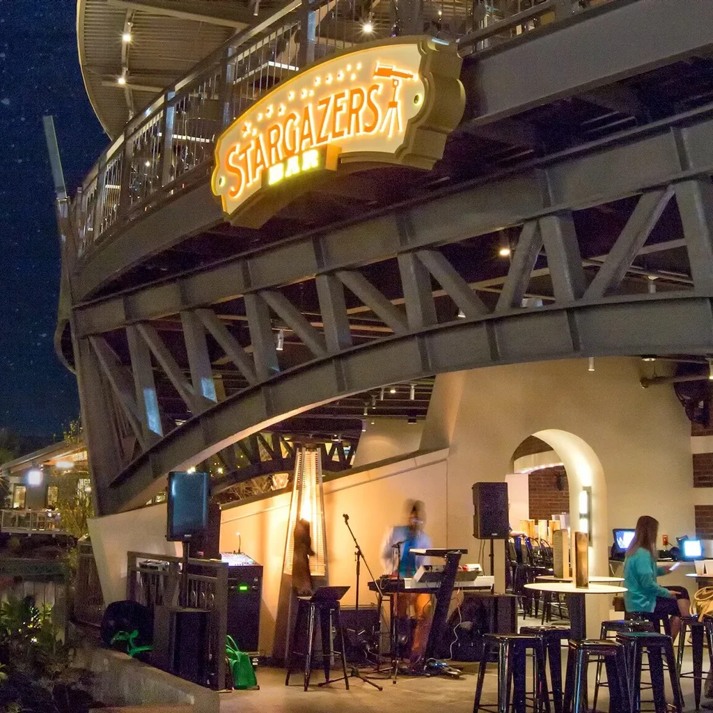 Illuminated Stargazers Bar sign and musician performing outdoors at night.