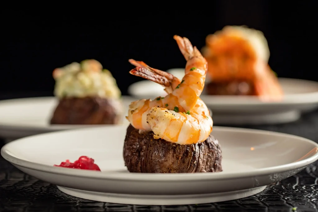 Seared tenderloin steak topped with two shrimp, chives, and red sauce.