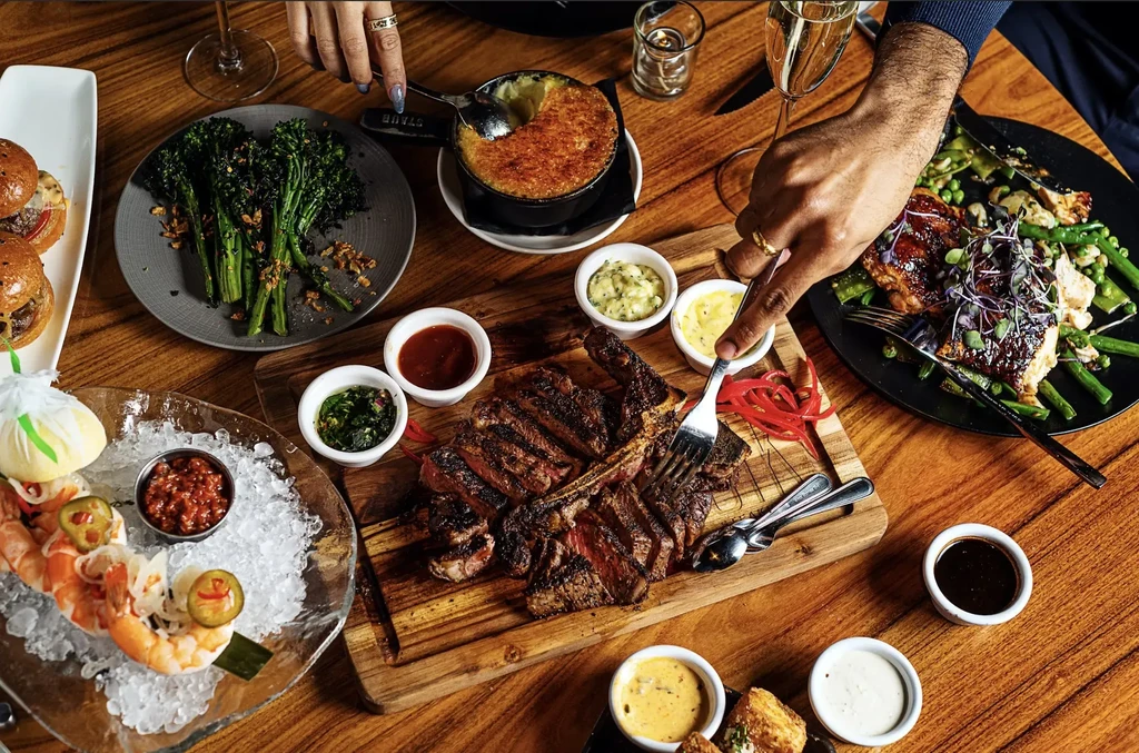Overhead: well-laden upscale dining table with steak, seafood, drinks.