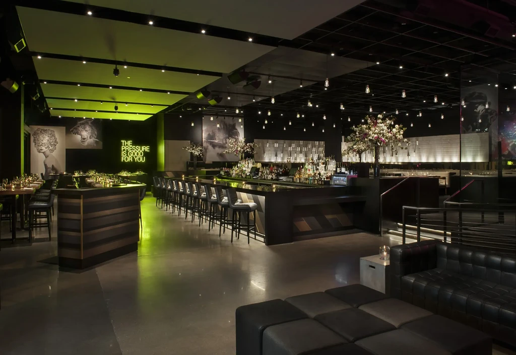 Empty modern restaurant bar, dark decor, green lighting, prominent neon sign.
