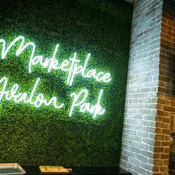 Green moss wall, 'Marketplace Avalon Park' neon sign, brick column, dark counter.