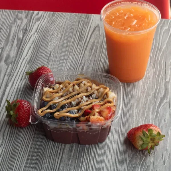 Overhead acai bowl with berries, granola, peanut butter, and orange drink.