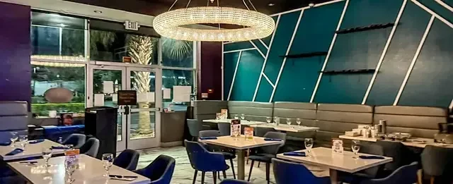 Modern restaurant interior, teal wall, crystal chandelier, set tables, night view.