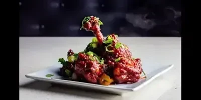 Reddish-brown glazed chicken lollipops with green onions on a white plate.