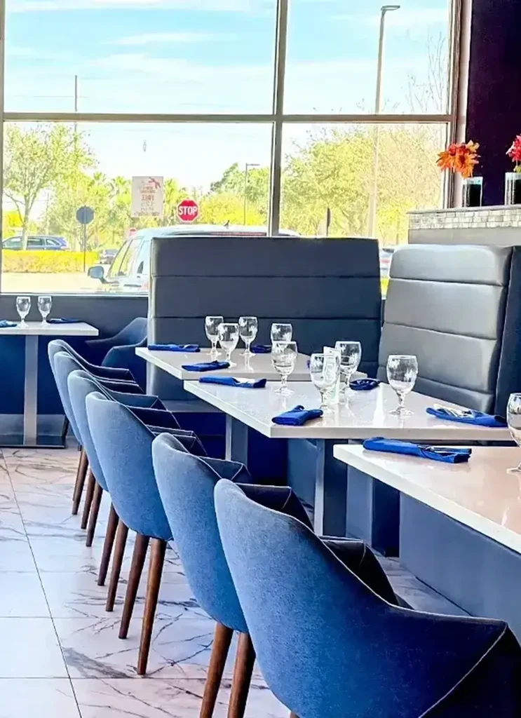 Modern restaurant interior with set tables, blue chairs, and window view.